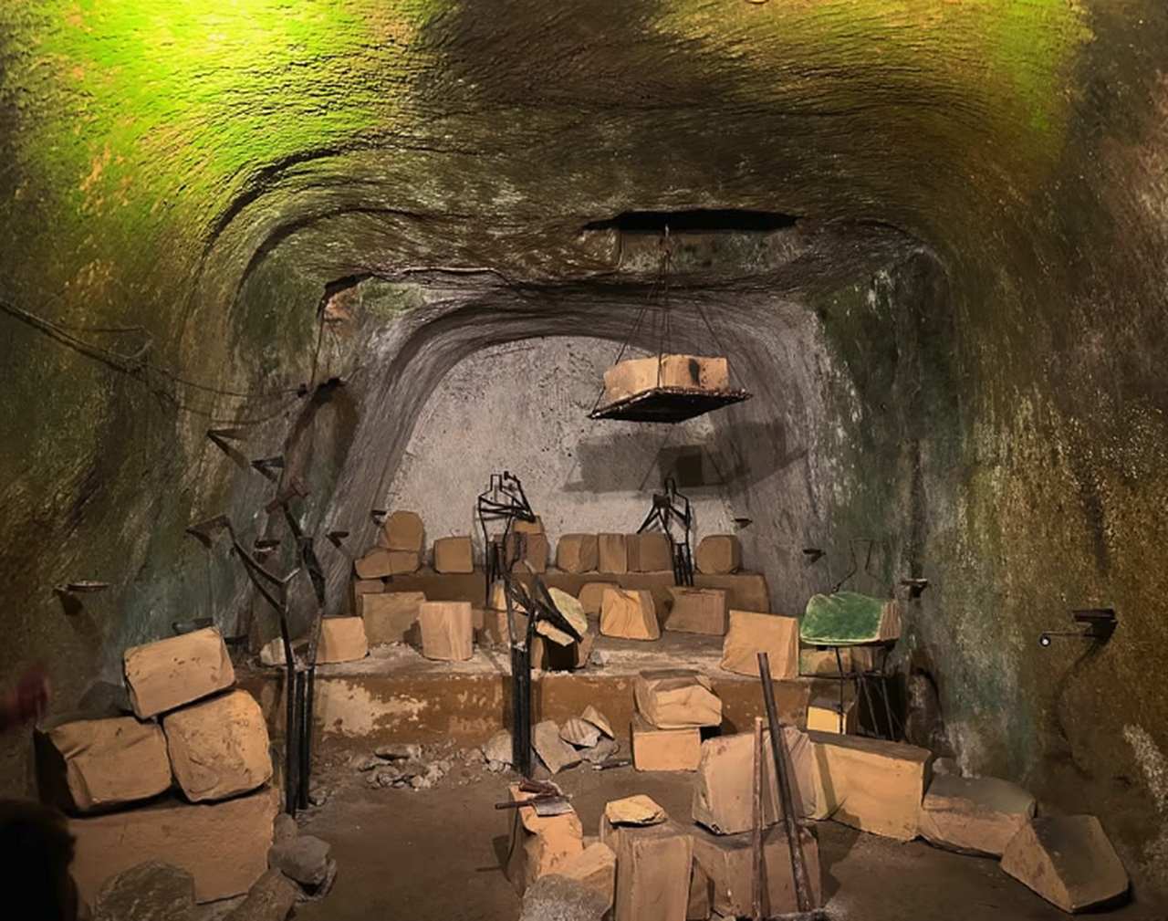 A lamp-lit chamber cut by hand out of the yellow tuff beneath Naples, blocks of quarried stone stacked across its floor